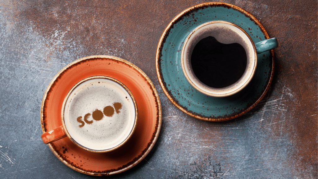 Cups filled with coffee, with with foam on the top with the word "scoop" sprinkled on in cinnamon.